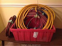 Photo showing multiple coiled pneumatic air hoses in red, yellow, and dark red colors stored inside a large red plastic tray on a table.