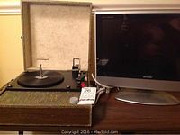 Sharp LCD TV monitor and vintage Silvertone travelling vinyl system side by side on table with power cords visible.