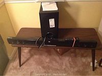 LG sound bar, subwoofer, remote, manual, and mounting bracket displayed on a wooden table in carpeted room.
