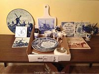Overall view of the Delft blue ceramics collection on a table in cardboard box, including plates, tiles, figurines, and shakers.