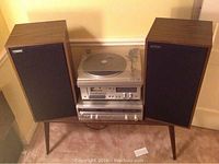Full view of the complete Fisher Studio-Standard stereo system including two tall speakers, stacked turntable, receiver, and tape deck units on a wooden stand.