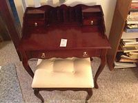 Full view of the dark wooden desk and matching upholstered stool placed on carpeted floor.