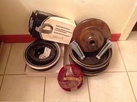 Photo of brake drums, relined brake shoes, brake disc, mounting brackets, and red light caps arranged on floor showing rust and aging.