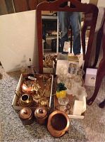 Photo of the mirror, brass birds and rooster, copper pot, lidded containers, various glass pieces and candle snuff holder on carpeted floor.