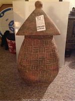 Front view of a large earthen container with lid, showing textured patterned surface and pointed lid top.