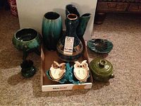Full view of the lot inside a cardboard box on carpet showing 10 blue-green ceramic items including vases, bowls, owl figurines, and serving dishes.
