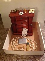 Full view of wooden jewelry box with multiple drawers and compartments, with assorted jewelry items displayed on and in front of it including faux pearl necklace, gold-tone watch, and bracelet.