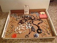 Photo shows multiple necklaces including white carved bead necklace, multi-colored bead necklaces, peace symbol pendant on black cord, and blue hoop earrings in the cardboard box.