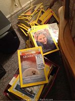 A pile of approximately 70 non-continuous National Geographic magazines dating back to the 1960s and 1970s, stacked on the floor with some covers visible showing wear and some missing covers.