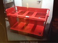 Front and top view showing an industrial heavy-duty red steel trolley with mesh grids and folding flat bars on top, used for securing items during transport.