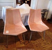 Pair of two mid-century fiberglass and metal chairs shown from front on hardwood floor under interior lighting.