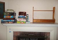 Photo showing a pile of family board games stacked next to the wooden shelf on a mantel.