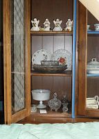 Cupboard shelf showing four Noel figurines with some damage, two Victoria Pottery dishes with floral and leaf designs, and rectangular glass dish.