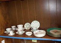 Shelved assortment of teacups, saucers, small plates, and larger dinner plates with floral patterns and some green rims.