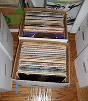 Two cardboard boxes filled with many vinyl records, seen from top-down view showing spines and covers.