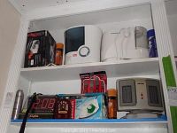 Shelf with Edgeware knife sharpener box, two humidifiers, Elgin digital alarm clock, and other housewares.