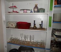 Shelf showing an array of glassware, ceramic items, and brass candle holders.