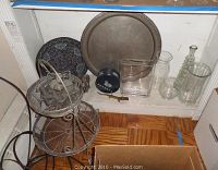 Photo of two brass trays, enameled tray, wire basket stand, elephant figurine, alligator nutcracker, glass bottles, and a key on the floor