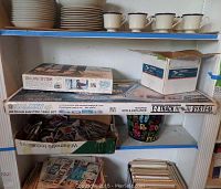 Shelf with boxes and items including the Revell USS Constitution ship model kit box on top, the Bachmann Galaxy HO scale electric train set box below, and a small box with assorted Legos and sports cards.