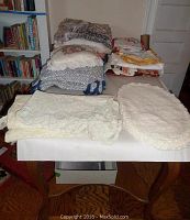 Photo of table with folded assorted table linens showing lace-edged placemats and various cloth items stacked