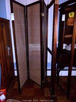 View of two three-panel room dividers standing side by side, dark wood frames with light wicker weave screens.