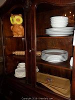 Owl cookie jar atop a wooden shelf alongside stacks of china plates and bowls and wooden trays below