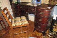 Front angle view of the wooden knee hole desk with the small chair beside it, clearly showing the seven drawers and brass-pull hardware.