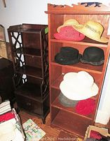 View of two wooden shelving units standing side by side. Smaller unit with drawer on the left and taller unit with hats on shelves on the right.