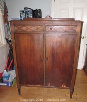 Front view of the small wooden wardrobe showing two doors and two drawers with carved diamond pattern, some finish wear and chipping at the bottom.