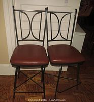 Front view of two metal bar stools with padded vinyl seats and cast iron style backs.