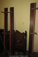 Two matching sets of dark wooden single bed frames, showing headboards with classic turned post carvings, footboards, and rails with iron brackets.
