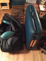 Photo showing folded green EarthLite massage table, padded armrest attachment inside black carrying bag, wood floor background.