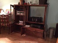 Front view of wooden entertainment hutch holding stereo equipment including cassette deck, CD player, and receiver with glass doors open and drawer partially open.