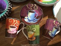 Four ceramic decorative coffee plates and three matching coffee mugs placed on a wooden table. One plate is chipped.