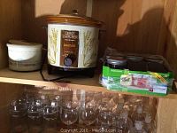 Photo shows brown and white Crockpot with wheat design, white ceramic queso pot with blue and red design, and 10 clear pint Mason jars with lids below shelf.