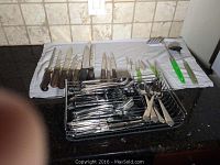 Photo of knives, forks, spoons, and utensils on kitchen counter with drying rack and towel