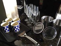 Photo showing 8 clear champagne flutes, 4 polka dot mugs (one cracked), 3 metal canisters with transparent lids, and a pancake skillet with metal handle.