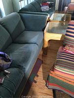 Blue-grey fabric sleeper sofa with bamboo trim and ripped middle seat cushion, matching bamboo side table with glass top.