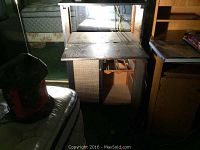 Vintage portable bar cabinet in dim lighting showing top section with fold-down shelf and wine bottle racks below