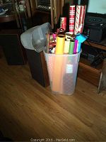 Photo of clear plastic storage bin filled with assorted rolls of wrapping paper in various holiday-themed and everyday patterns, next to its lid.