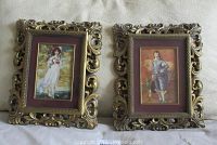 Pair of two ornate gold plastic framed prints sitting side by side on fabric background.