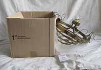 Photo of cardboard box alongside disassembled brass-finished chandelier frame