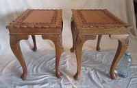 Front view of the pair of carved wooden side tables showing leaf carvings on legs and tops with scalloped edge detail.