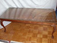 Full view of the wooden coffee table with fitted glass top, showing the carved leaf detail around the frame and legs.