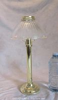 Full view of brass candle lamp with vertically ribbed glass shade and brass holder ring on top.