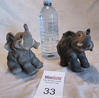 Photo showing front view of two ceramic elephant figurines next to a water bottle for size reference