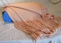 Full view of the folded light coral woven blanket showing thick twisted fringe ends.