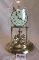 Front view of the Staiger Quartz dome clock inside an acrylic dome with gold-tone base and pillars.