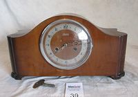 Front view of wooden mantel clock with key on cloth, clock face with Arabic numerals and glass cover closed.