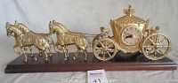 Full view of the horse and carriage clock, showing two horses connected by chains to an ornate carriage with clock in the center, all mounted on a wooden base.